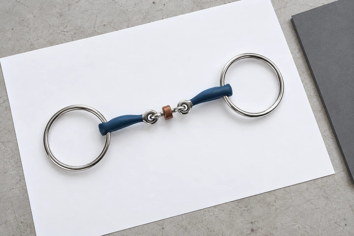 Complete loose-ring horse bit resting on a blank sheet beside a neutral folder