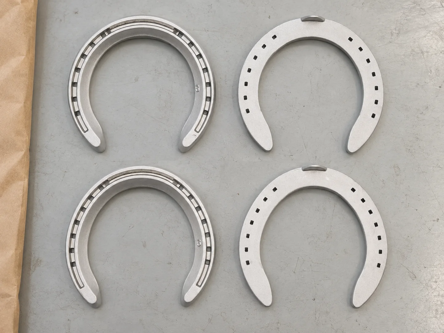 Four aluminum horseshoes arranged as individual pieces on a light packing table