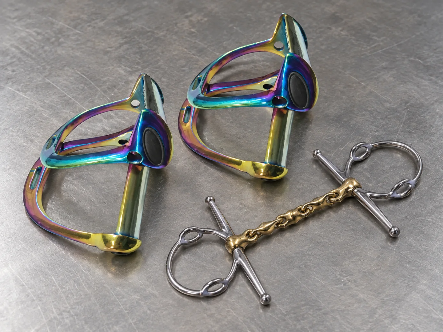 Rainbow-finish riding stirrups and a full-cheek horse bit arranged on a sample table