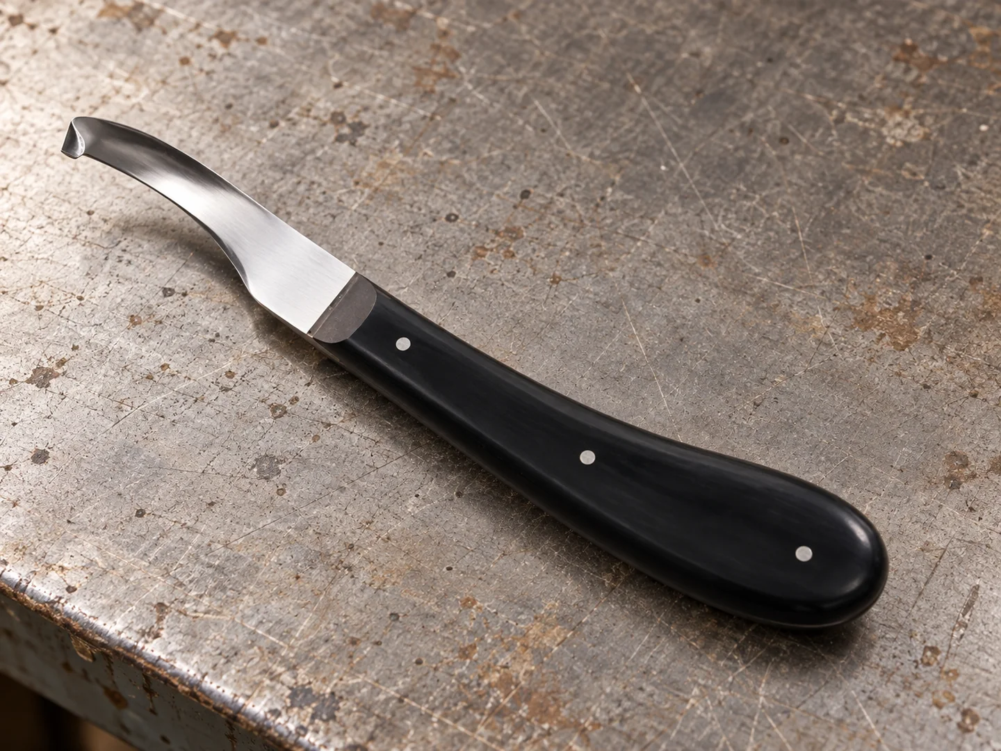 Curved hoof knife showing its black handle, fixing pins and hooked blade