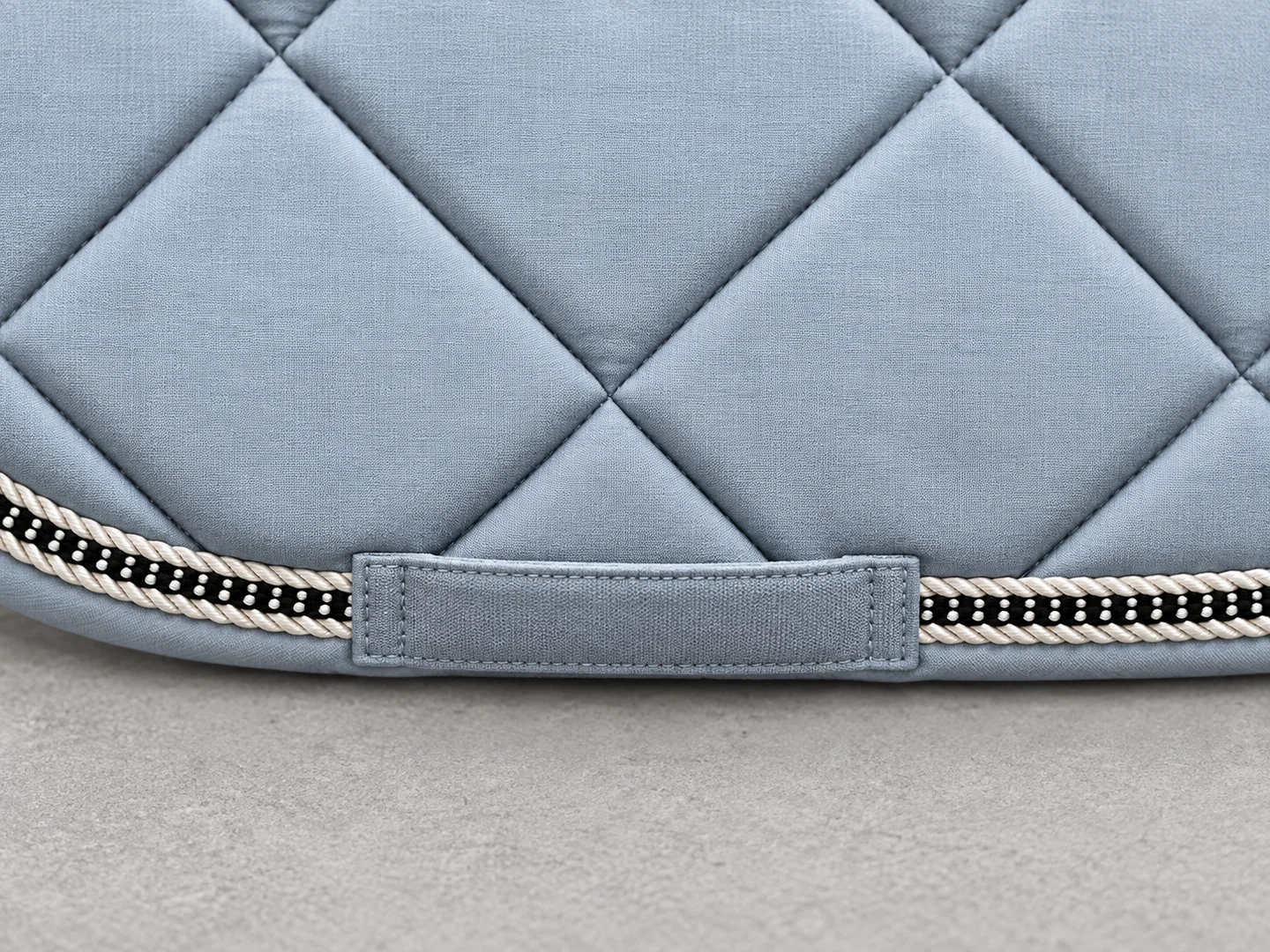 Lower attachment loop and bound edge of a blue-grey quilted saddle pad